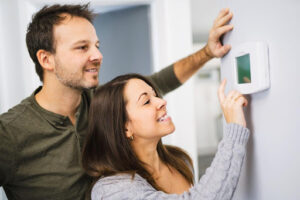 A man and woman adjusting a thermostat in a home.