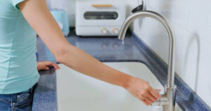 A woman turning on a sink faucet in a kitchen.