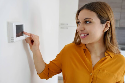 A smiling woman adjusting a thermostat.