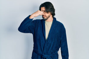 A man in a bath robe holding his nose.