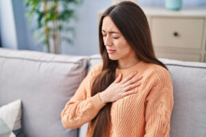 A woman having trouble breathing as she sits on a couch in a home.