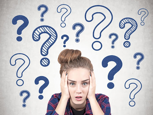 Woman holding her head in her hands while surrounded by question marks.